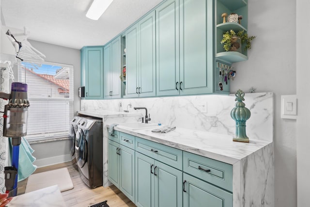 clothes washing area featuring cabinet space, baseboards, light wood-style flooring, washer and dryer, and a sink