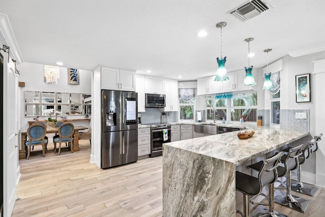 kitchen featuring decorative light fixtures, stainless steel appliances, visible vents, white cabinets, and a peninsula