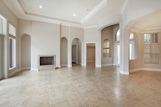 unfurnished living room featuring a high ceiling, a tray ceiling, a high end fireplace, and crown molding