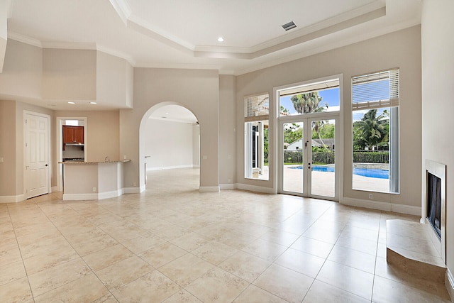 unfurnished living room with a towering ceiling, french doors, a raised ceiling, and crown molding