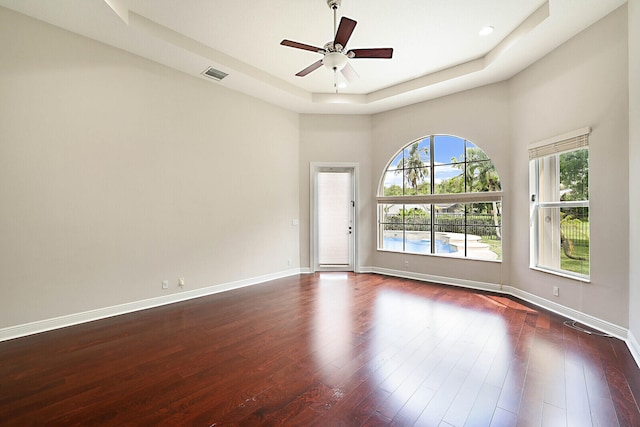 unfurnished room with ceiling fan, dark wood-type flooring, and a tray ceiling