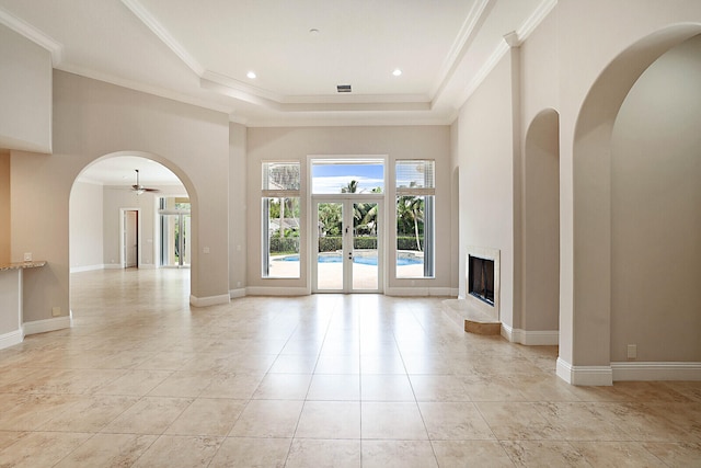 unfurnished living room with crown molding, a raised ceiling, french doors, light tile patterned floors, and a high ceiling