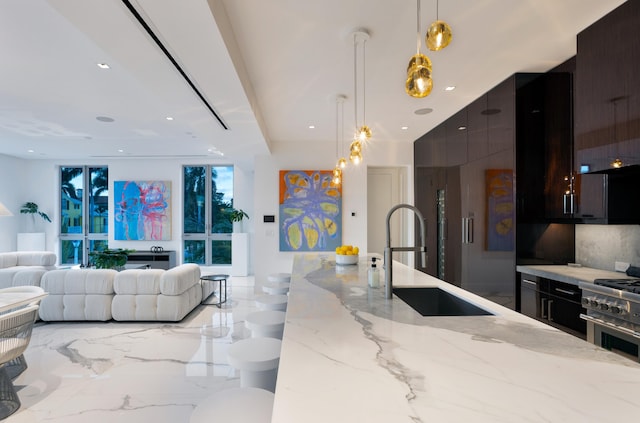 kitchen with sink, light stone counters, decorative light fixtures, dark brown cabinets, and stainless steel range