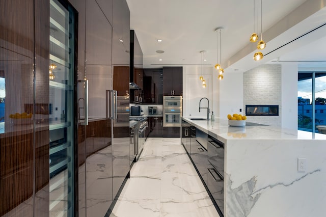 kitchen with a fireplace, sink, hanging light fixtures, a large island with sink, and light stone countertops