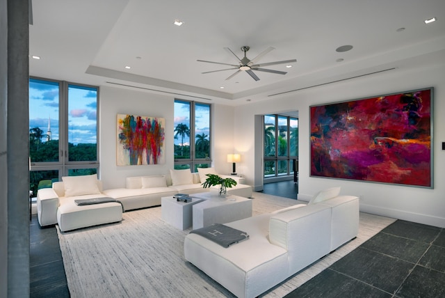 living room with a tray ceiling, floor to ceiling windows, and ceiling fan