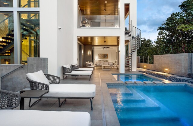 pool at dusk with a patio, outdoor lounge area, and ceiling fan