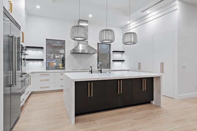 kitchen with light hardwood / wood-style floors, white cabinetry, hanging light fixtures, and a kitchen island with sink