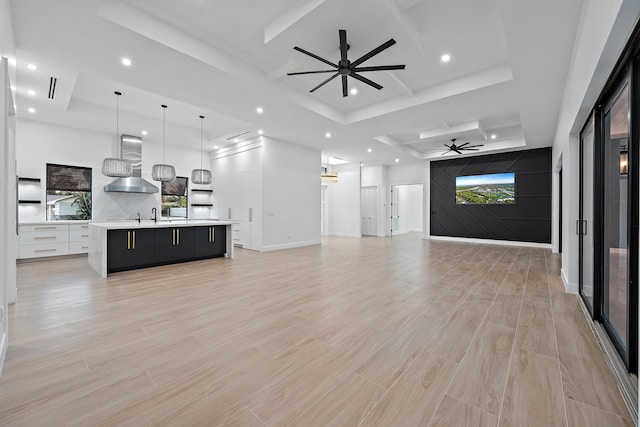 unfurnished living room with a raised ceiling, ceiling fan, light hardwood / wood-style flooring, and a healthy amount of sunlight