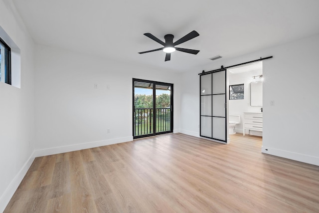 unfurnished bedroom featuring ceiling fan, a barn door, access to exterior, light wood-type flooring, and connected bathroom