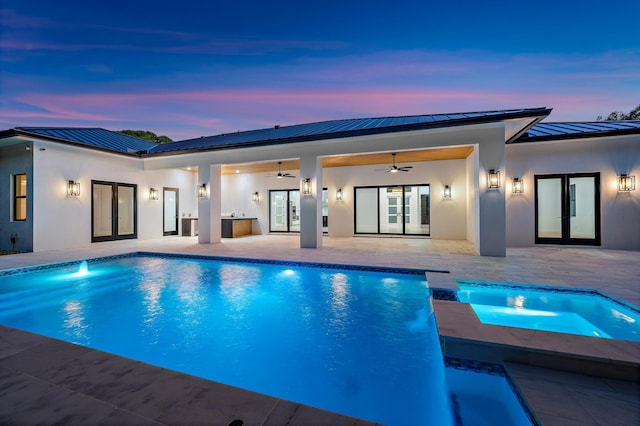 pool at dusk with an in ground hot tub, french doors, ceiling fan, and a patio area