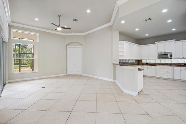 kitchen with light tile patterned floors, ornamental molding, kitchen peninsula, and white cabinets