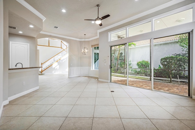 tiled spare room featuring ceiling fan with notable chandelier, ornamental molding, and a textured ceiling