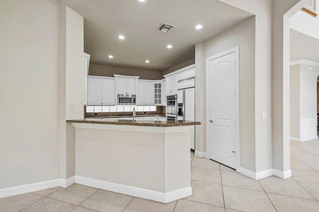 kitchen featuring white cabinetry, light tile patterned flooring, dark stone countertops, and kitchen peninsula