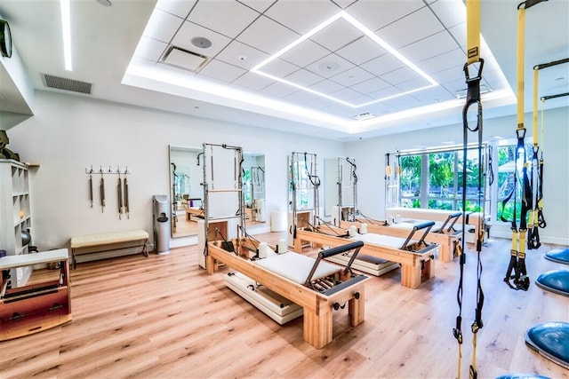 exercise room with a drop ceiling, light wood-type flooring, and a tray ceiling