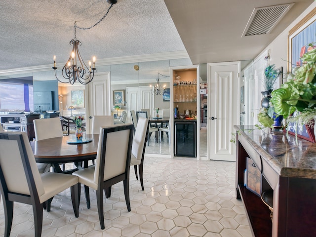 tiled dining area with a textured ceiling, ornamental molding, a chandelier, and wine cooler