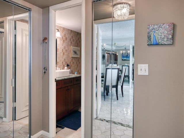 corridor with sink, ornamental molding, a chandelier, and light tile patterned flooring