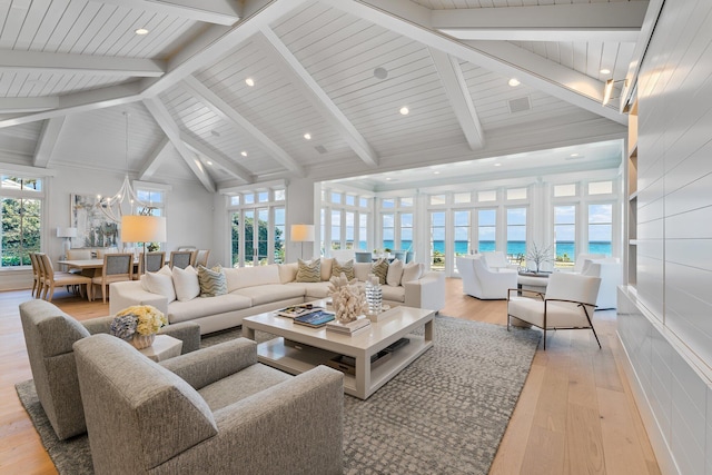 living room featuring beamed ceiling, light hardwood / wood-style floors, a water view, and plenty of natural light