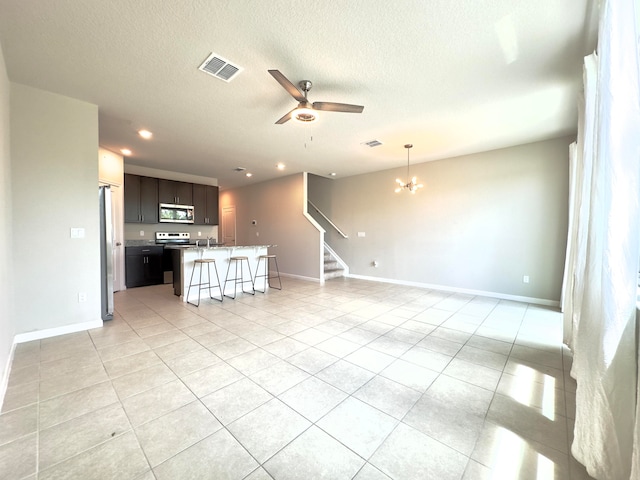 unfurnished living room with ceiling fan with notable chandelier, light tile patterned floors, and a textured ceiling