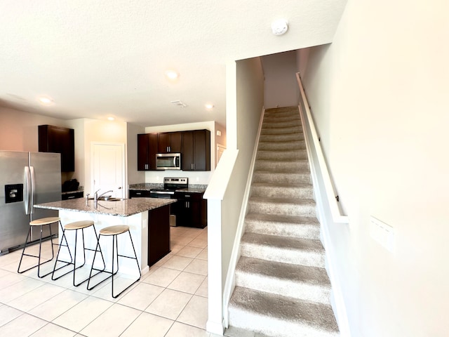 kitchen with appliances with stainless steel finishes, a breakfast bar area, dark brown cabinets, a kitchen island with sink, and light tile patterned flooring