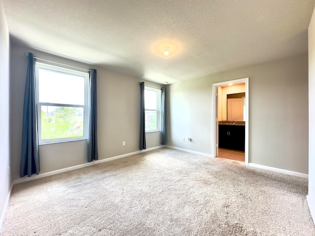 unfurnished bedroom featuring connected bathroom, light colored carpet, and a textured ceiling