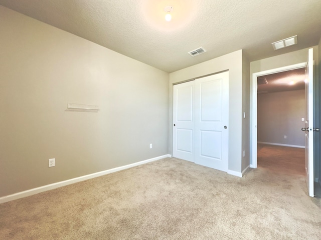 unfurnished bedroom featuring a closet, a textured ceiling, and light colored carpet