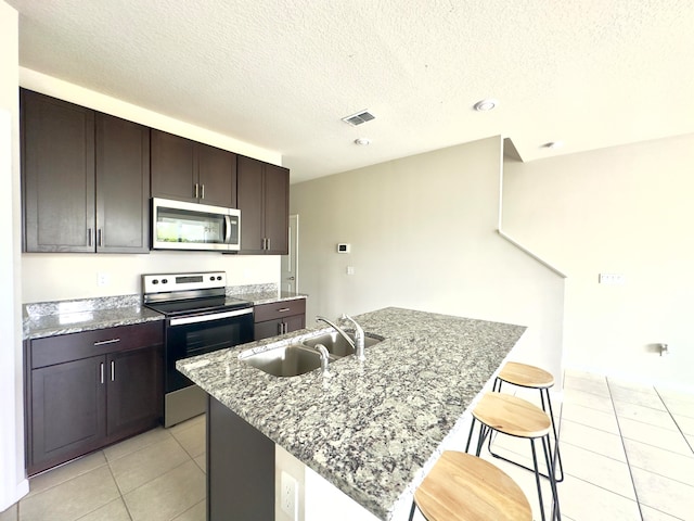 kitchen featuring light tile patterned floors, stainless steel appliances, sink, a kitchen breakfast bar, and a center island with sink