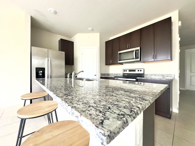 kitchen with dark stone counters, sink, a center island with sink, a breakfast bar, and appliances with stainless steel finishes