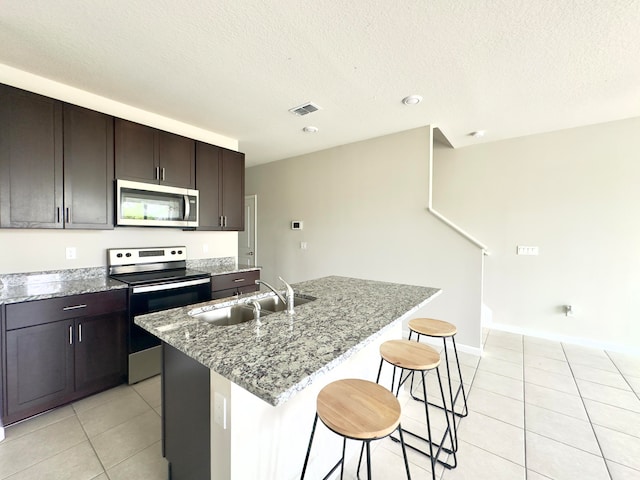 kitchen featuring stainless steel appliances, sink, stone countertops, an island with sink, and light tile patterned flooring