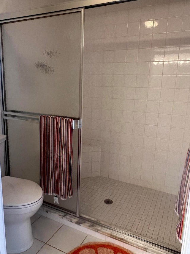 bathroom with a shower with shower door, tile patterned flooring, and toilet