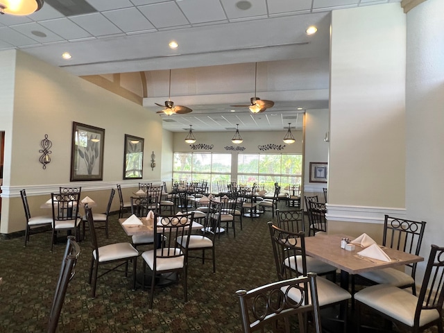 carpeted dining space with ceiling fan, a paneled ceiling, and a high ceiling