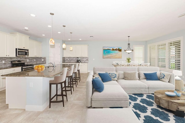 interior space with backsplash, dark stone countertops, appliances with stainless steel finishes, and an island with sink