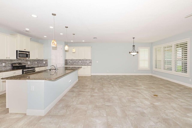 kitchen featuring tasteful backsplash, baseboards, appliances with stainless steel finishes, dark stone countertops, and a kitchen island with sink