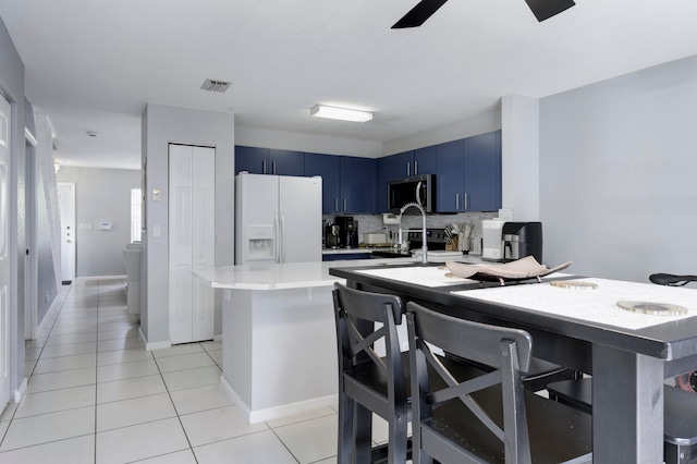 kitchen featuring tasteful backsplash, ceiling fan, white refrigerator with ice dispenser, blue cabinetry, and kitchen peninsula