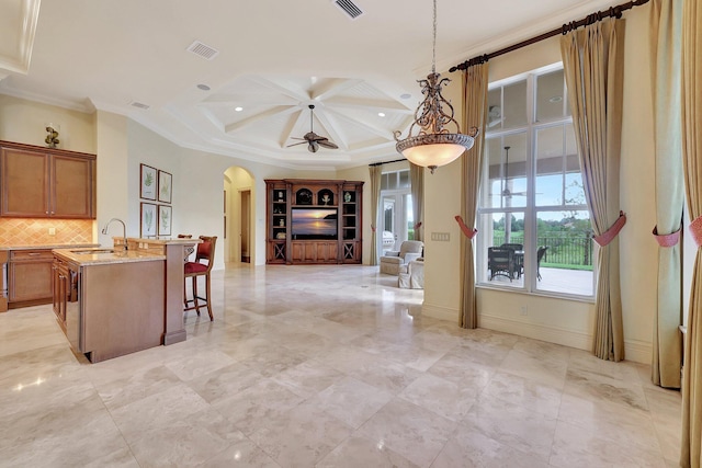 kitchen featuring sink, ceiling fan, crown molding, light stone countertops, and decorative light fixtures