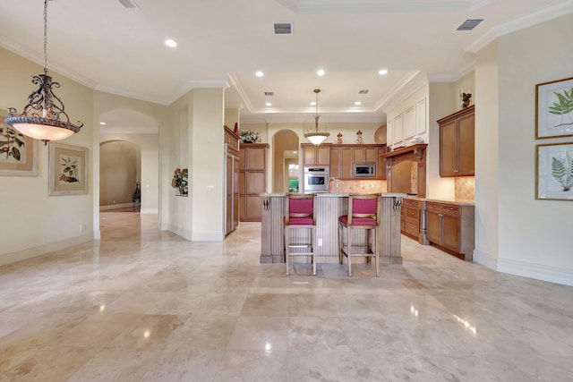 kitchen featuring stainless steel appliances, hanging light fixtures, a center island with sink, and ornamental molding