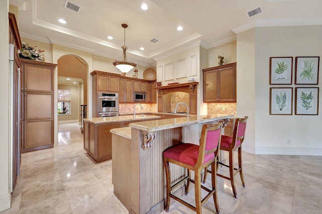 kitchen featuring stainless steel appliances, an island with sink, a kitchen breakfast bar, crown molding, and decorative light fixtures