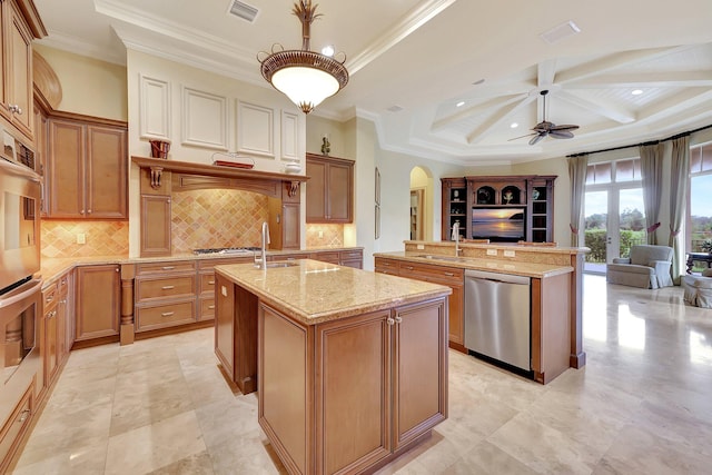 kitchen with beamed ceiling, light stone counters, appliances with stainless steel finishes, ornamental molding, and an island with sink