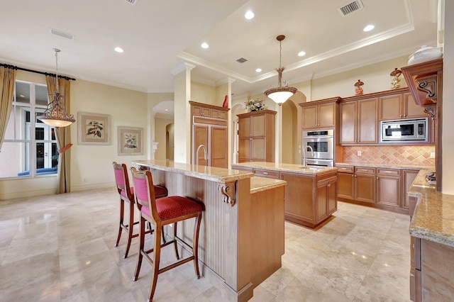 kitchen featuring built in appliances, a large island with sink, decorative light fixtures, and a breakfast bar