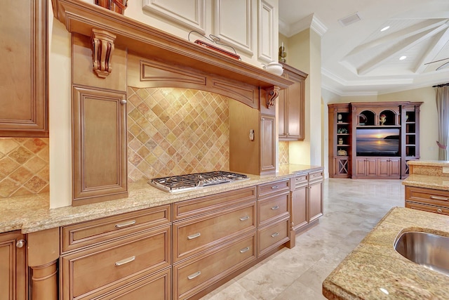 kitchen with light stone countertops, stainless steel gas cooktop, decorative backsplash, and ornamental molding