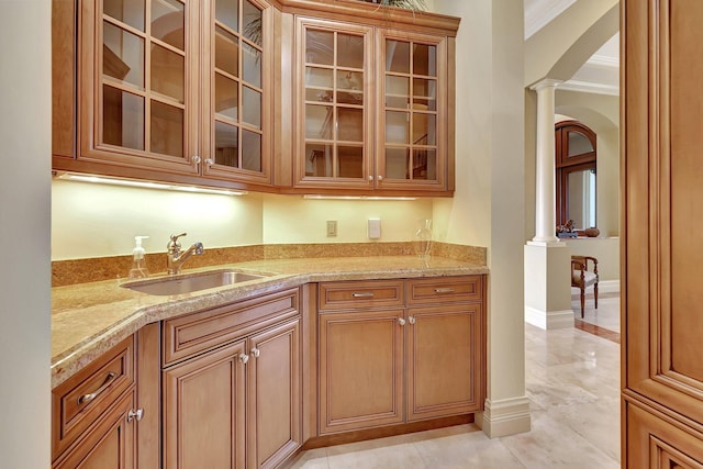 kitchen featuring light stone countertops, decorative columns, sink, and ornamental molding