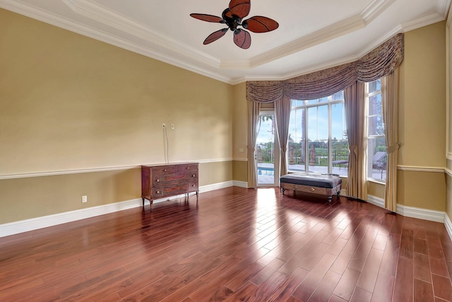 empty room featuring dark wood-type flooring, ceiling fan, ornamental molding, and a raised ceiling