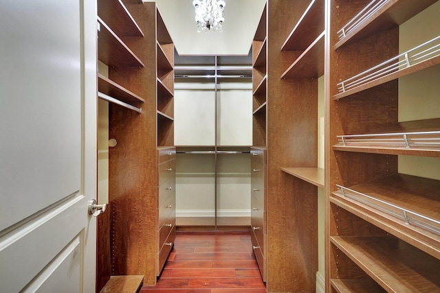 spacious closet with dark wood-type flooring and an inviting chandelier