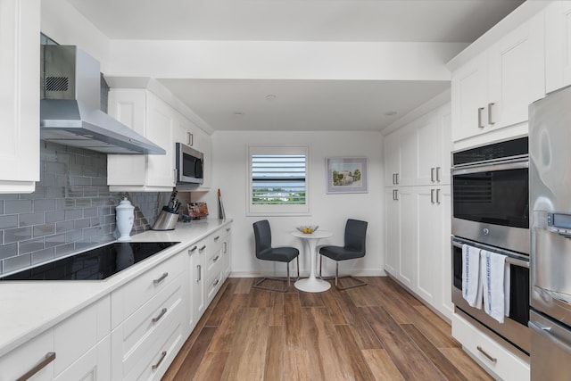 kitchen with wall chimney range hood, dark hardwood / wood-style flooring, white cabinets, stainless steel appliances, and backsplash