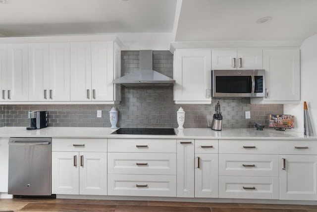 kitchen featuring tasteful backsplash, wall chimney range hood, white cabinetry, and appliances with stainless steel finishes