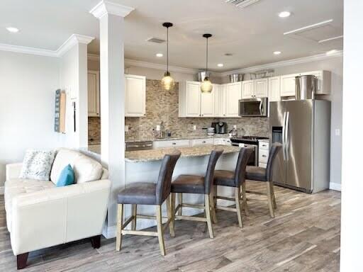 kitchen with light stone counters, hanging light fixtures, ornamental molding, appliances with stainless steel finishes, and backsplash