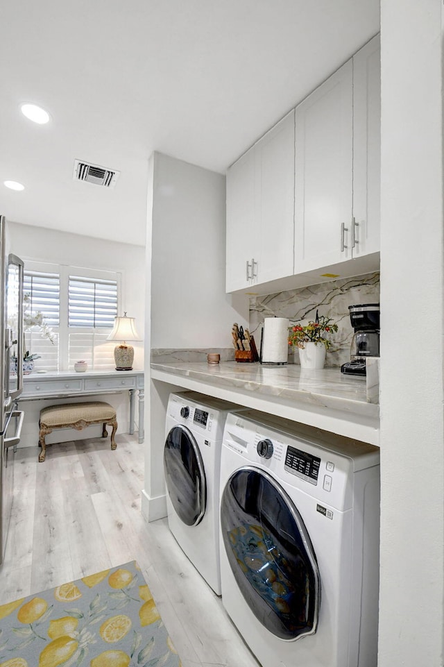 laundry area featuring independent washer and dryer, light wood-type flooring, and cabinets