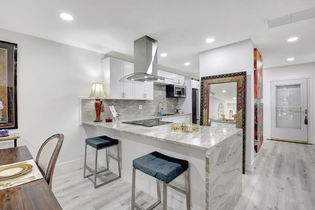 kitchen with kitchen peninsula, white cabinets, light stone countertops, and island range hood