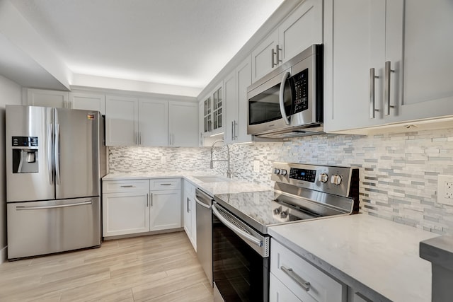 kitchen featuring stainless steel appliances, decorative backsplash, light wood-type flooring, sink, and light stone countertops