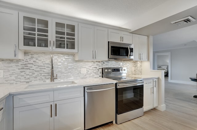 kitchen featuring stainless steel appliances, white cabinets, decorative backsplash, sink, and light hardwood / wood-style floors