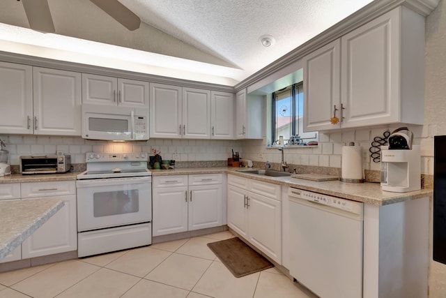 kitchen with sink, white appliances, white cabinetry, light tile patterned flooring, and vaulted ceiling